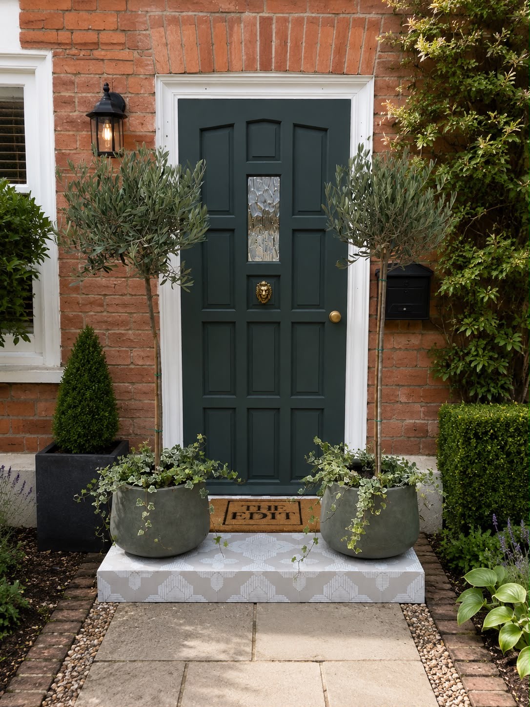 Olive trees in stone planters framing a dark green front door